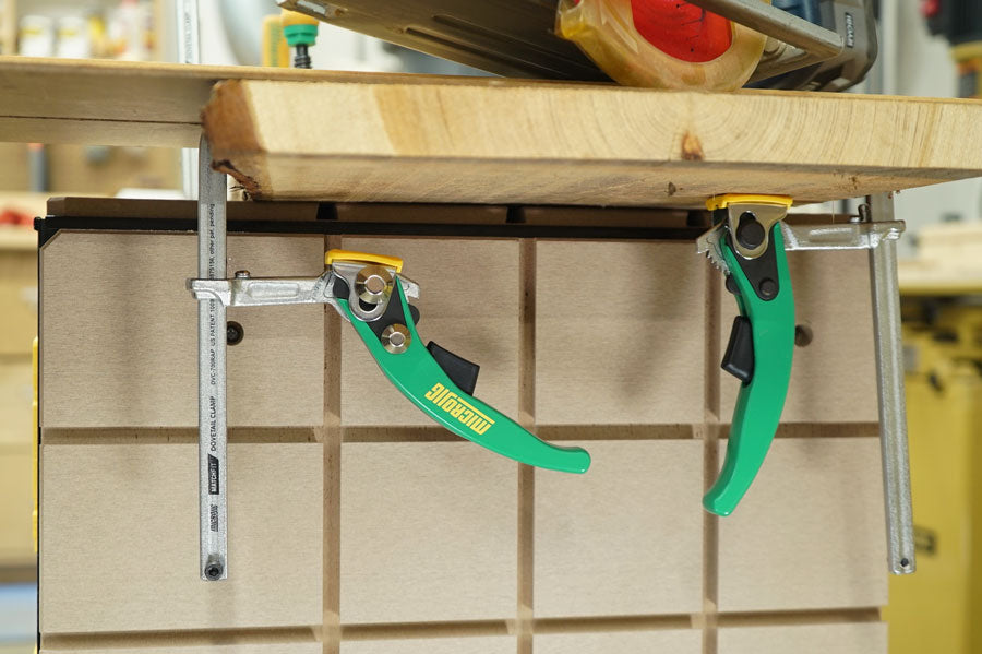 Workbench with two green lever woodworking clamps securing a wooden board