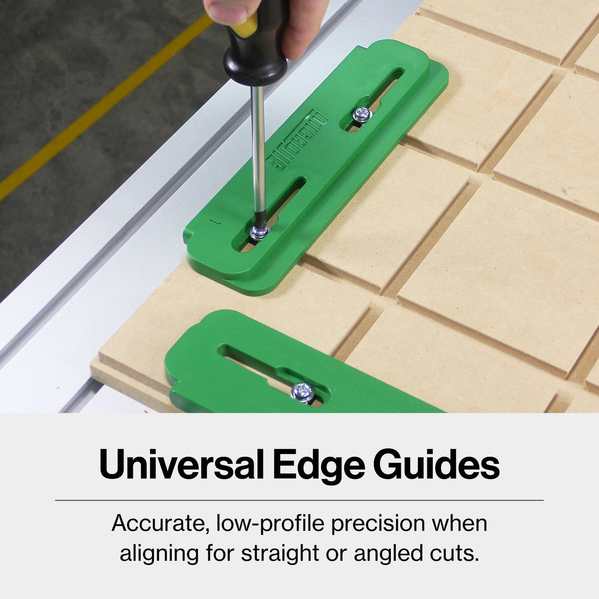 Green universal edge guides being adjusted with a screwdriver on a woodworking table.