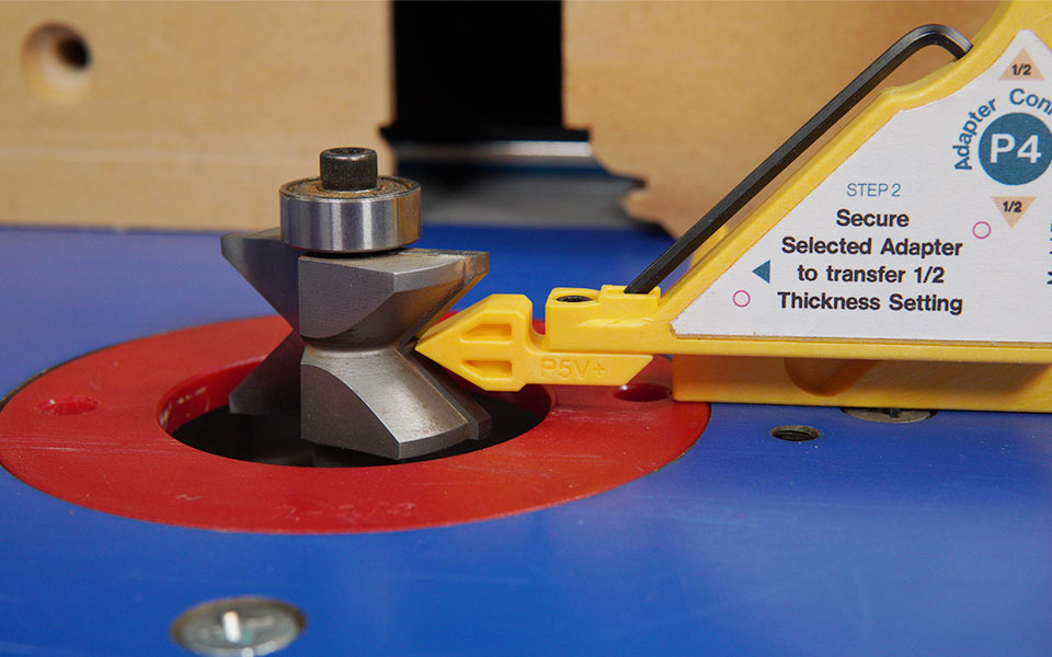 Close-up of woodworking router bit with setup gauge on blue router table surface