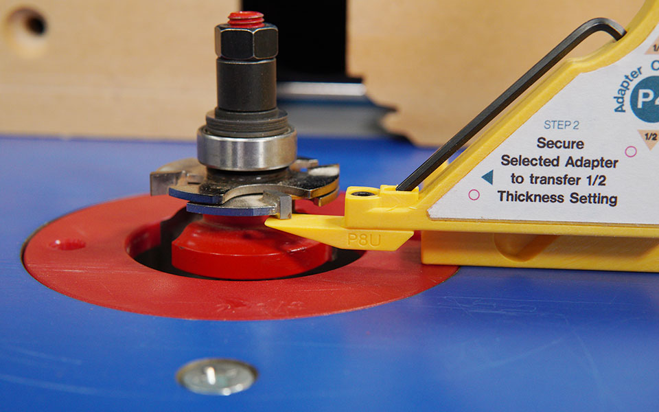 Close-up of a woodworking router bit and thickness setting jig on a router table.