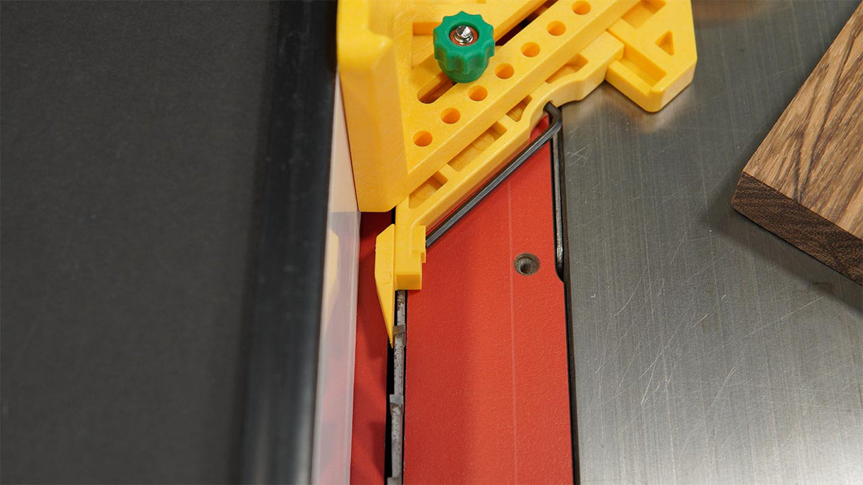 Table saw with red blade insert, yellow safety jig, and wood piece for precise woodworking