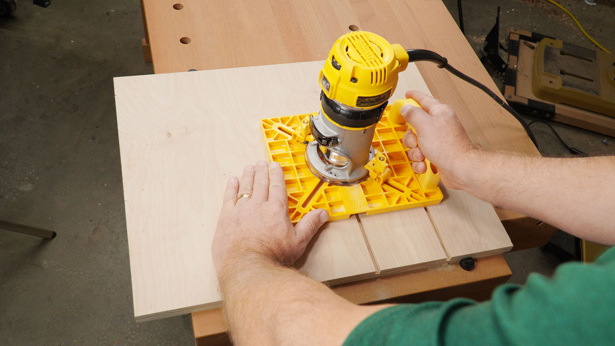 Woodworker using a handheld router with a yellow guide on a wooden board for precise grooving.