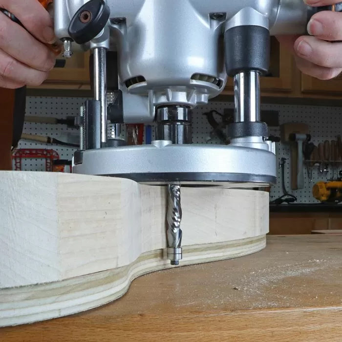 Woodworker using a plunge router with straight bit to shape hardwood on workbench