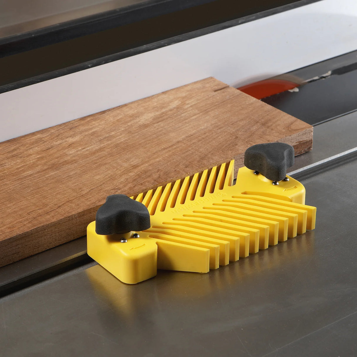 Yellow table saw featherboard securing wood for safe, precise woodworking cuts.
