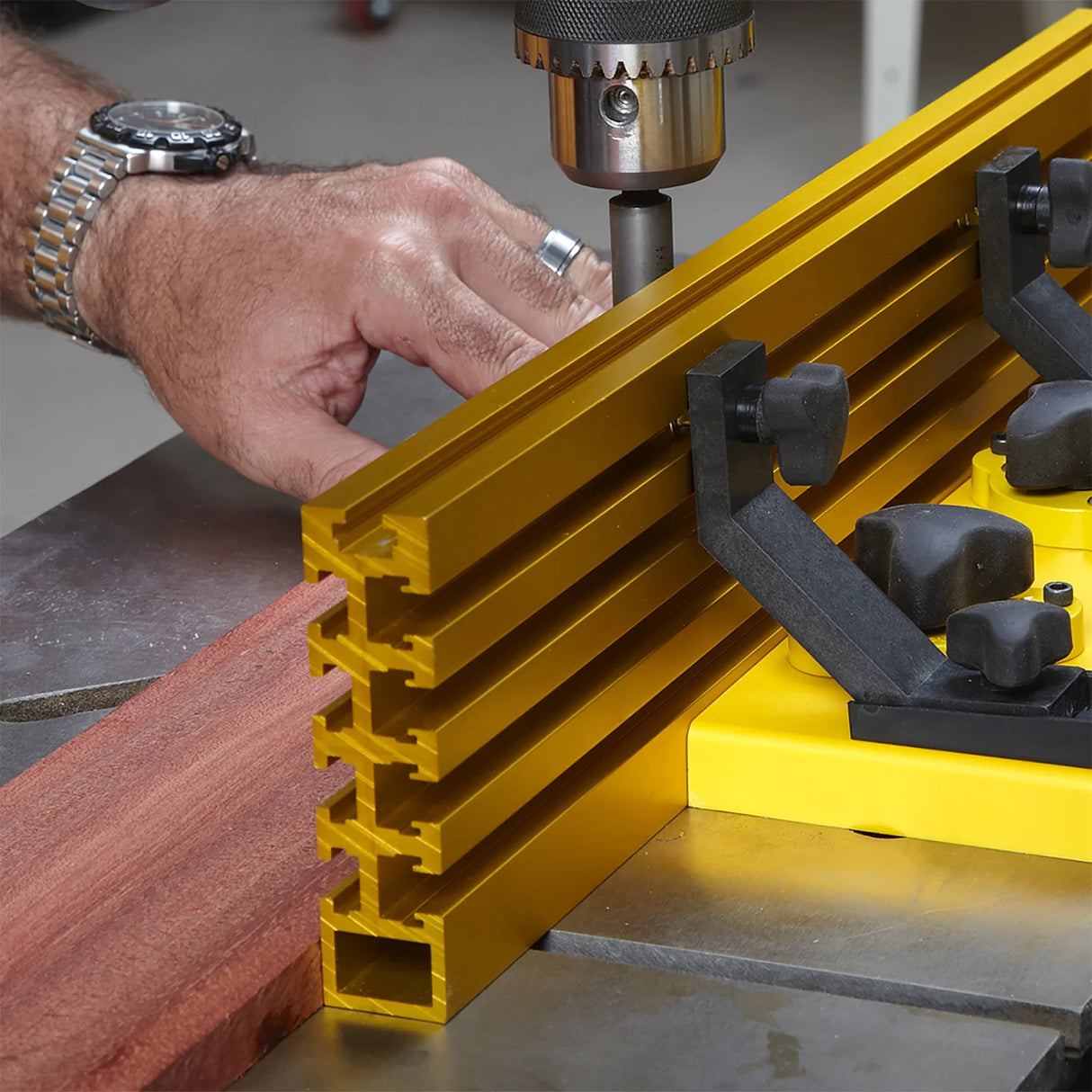 Person using a drill press with a gold aluminum fence and clamping system for woodworking