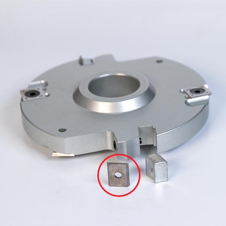Close-up of a metal woodworking cutter head with carbide insert and spare insert highlighted