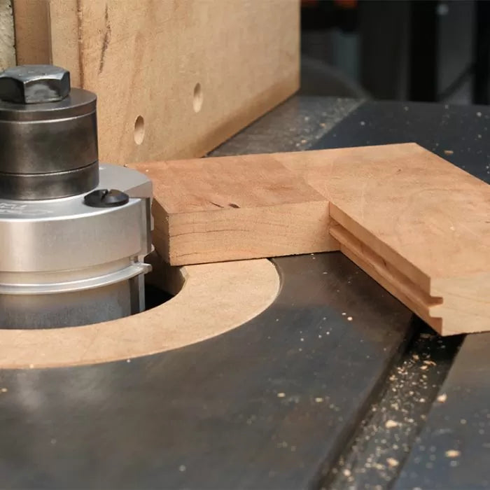 Router table cutting groove joints in wooden boards, woodworking tool in action.