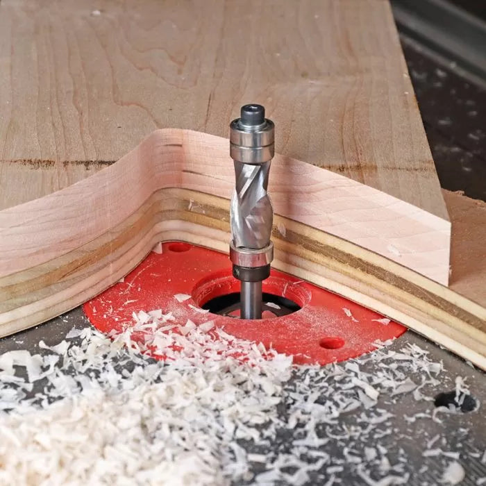 Router bit cutting curved wood edge on red router table with wood shavings