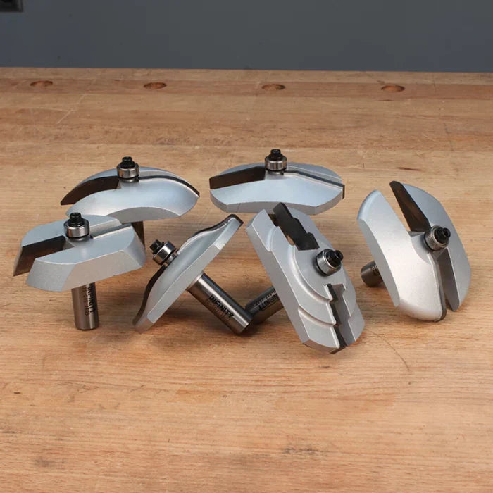 Set of silver woodworking router bits with ball bearings on a wood workbench