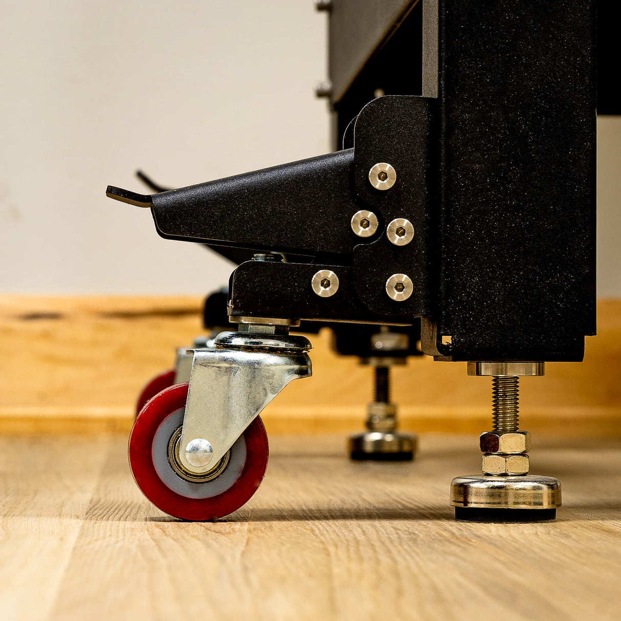 Close-up of adjustable router table leg with red caster wheel and leveling foot on wood floor