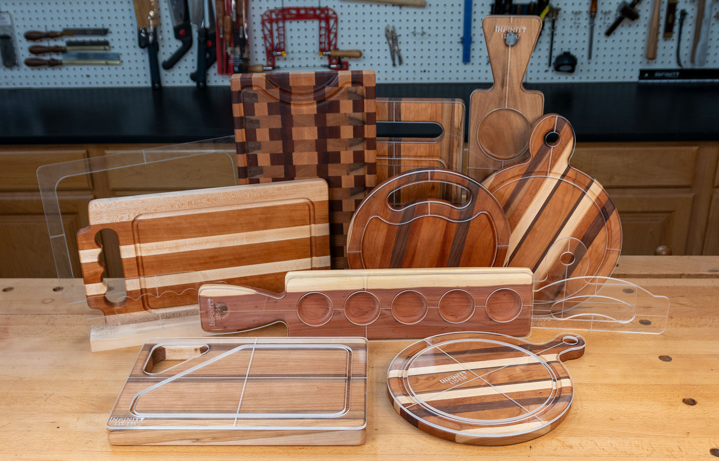 Acrylic cutting board templates displayed over various wooden cutting boards in a woodworking shop.
