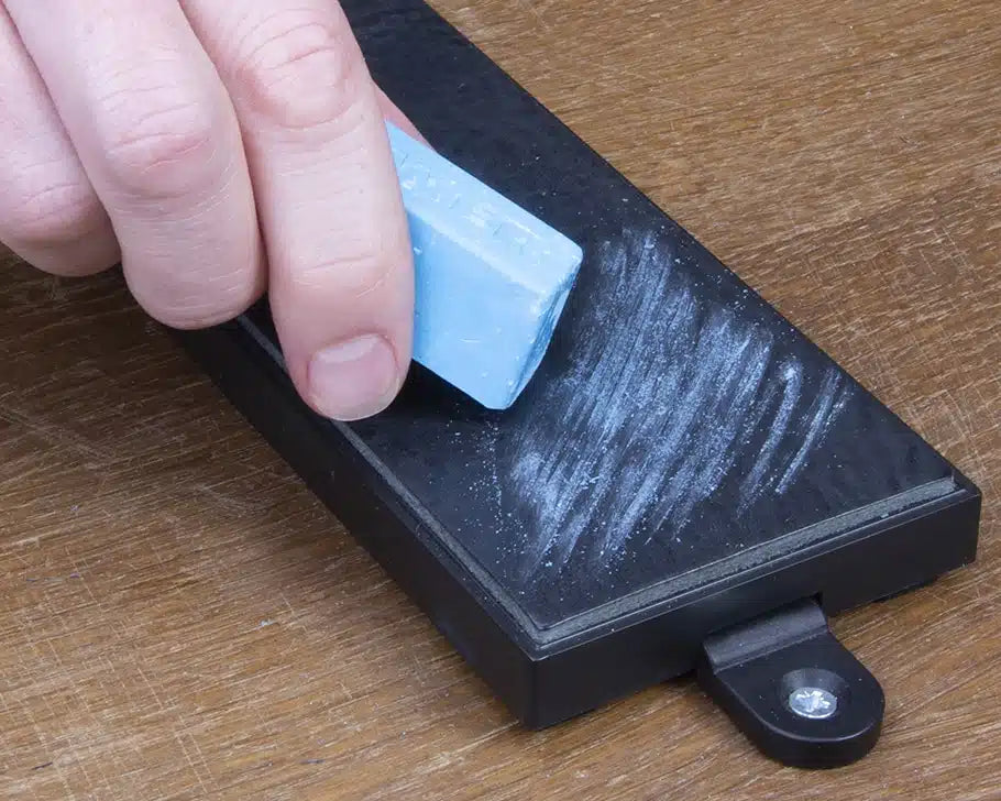 Hand applying blue wax to sharpening stone for woodworking tool maintenance
