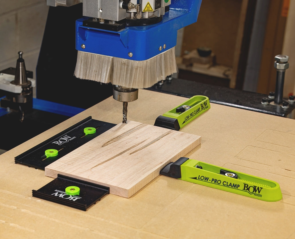 CNC machine routing wood panel secured by low-profile woodworking clamps