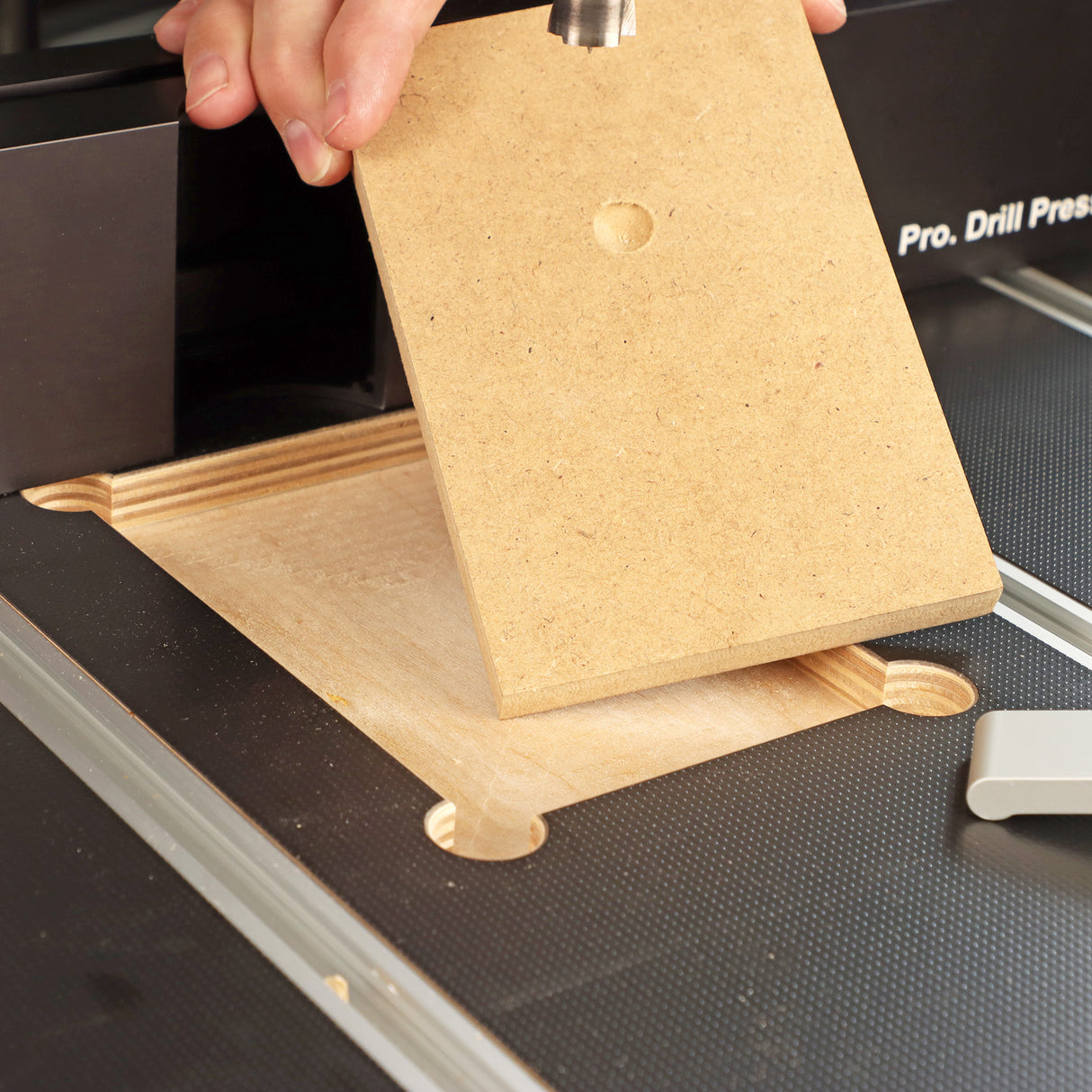 Drill press table with replaceable MDF insert and woodworker's hand during woodworking setup
