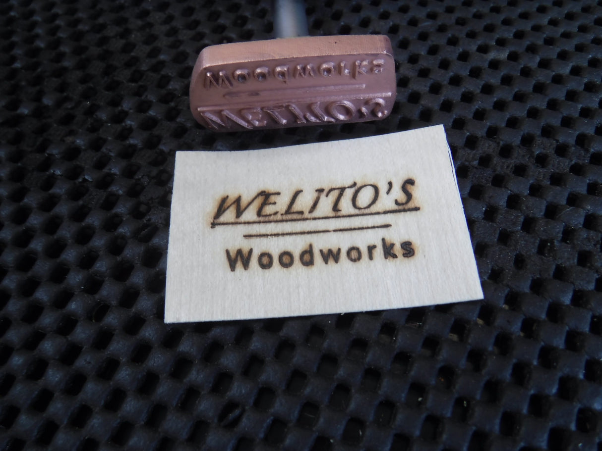 Custom wood branding iron and branded wood tag reading 'WELITO'S Woodworks' on black mat
