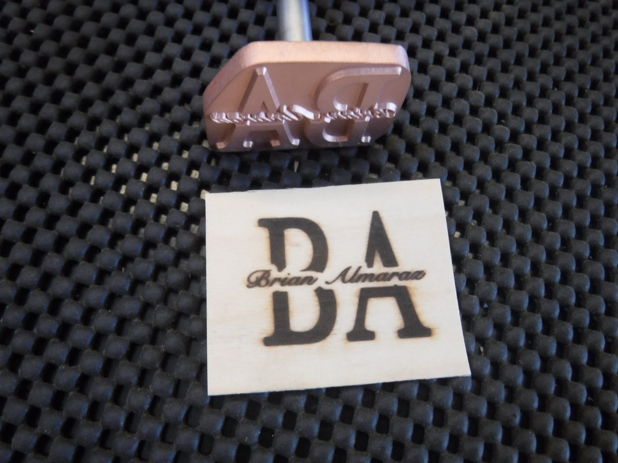 Custom metal branding iron tool with branded wood sample on textured black mat