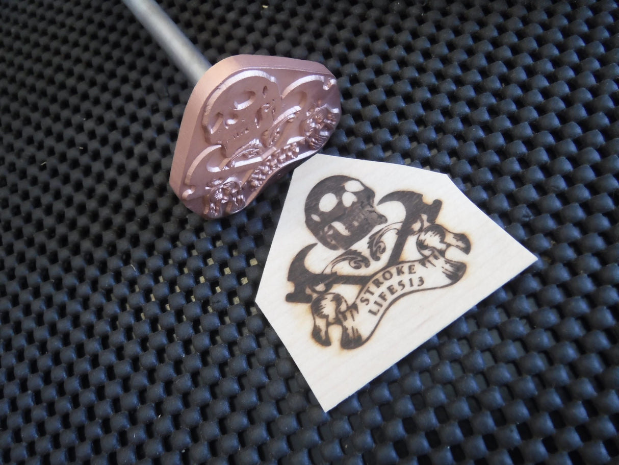 Metal branding iron with skull design and wood burned logo on textured black mat
