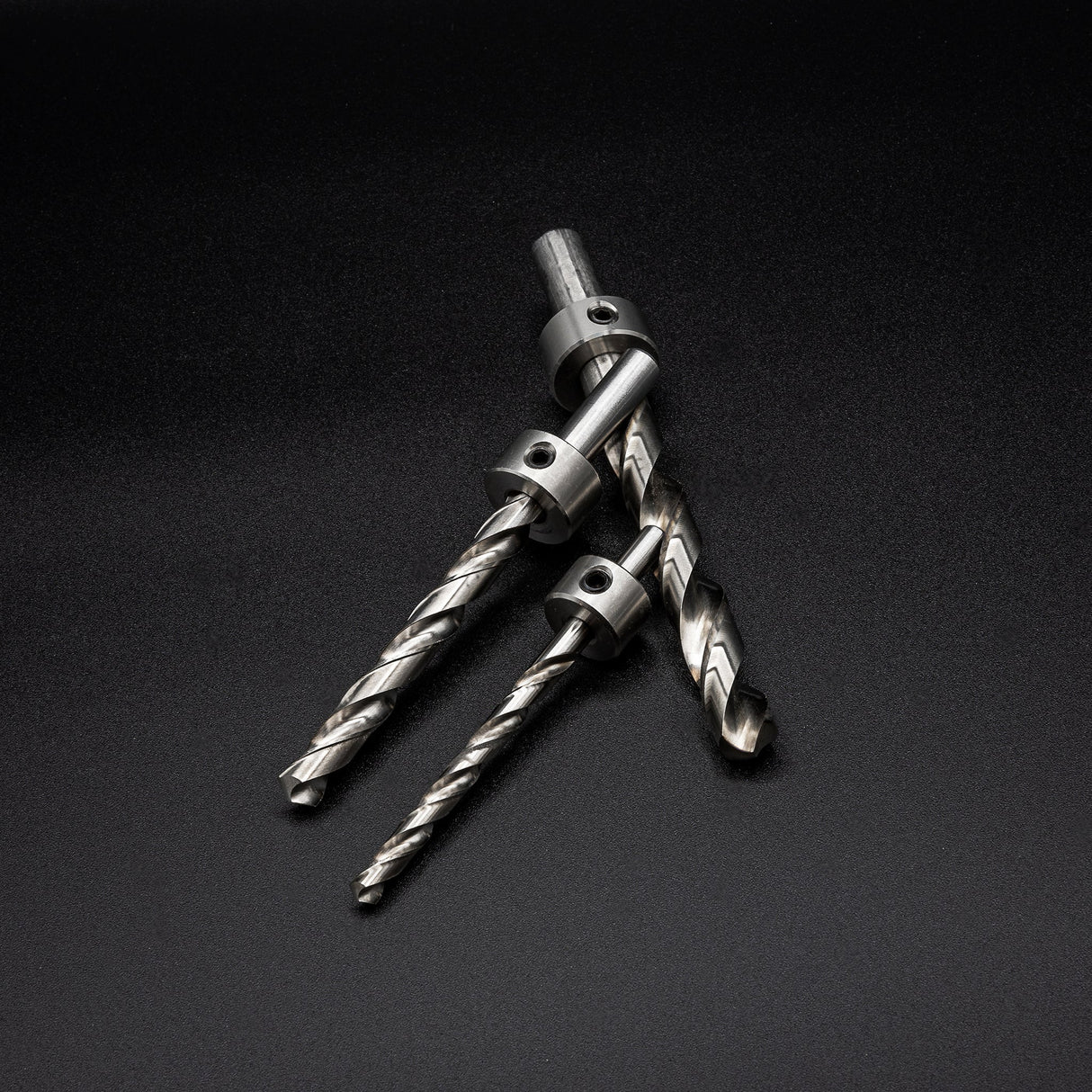 Three metal drill bits with stop collars on a black background, woodworking tool closeup