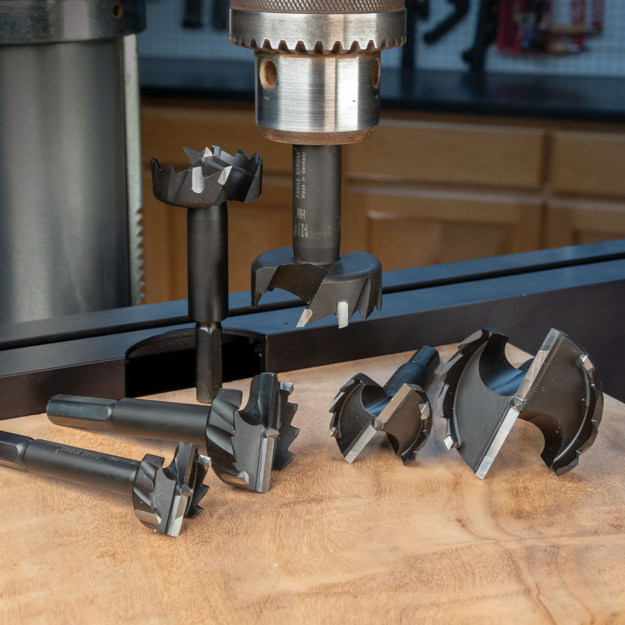 Assorted Forstner drill bits displayed on a wood surface, one mounted in a drill press