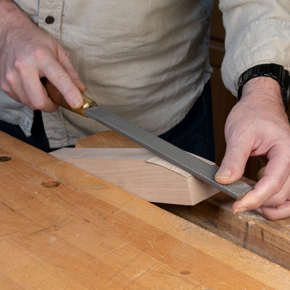 Woodworker using a hand rasp file to shape a wood piece on a workbench