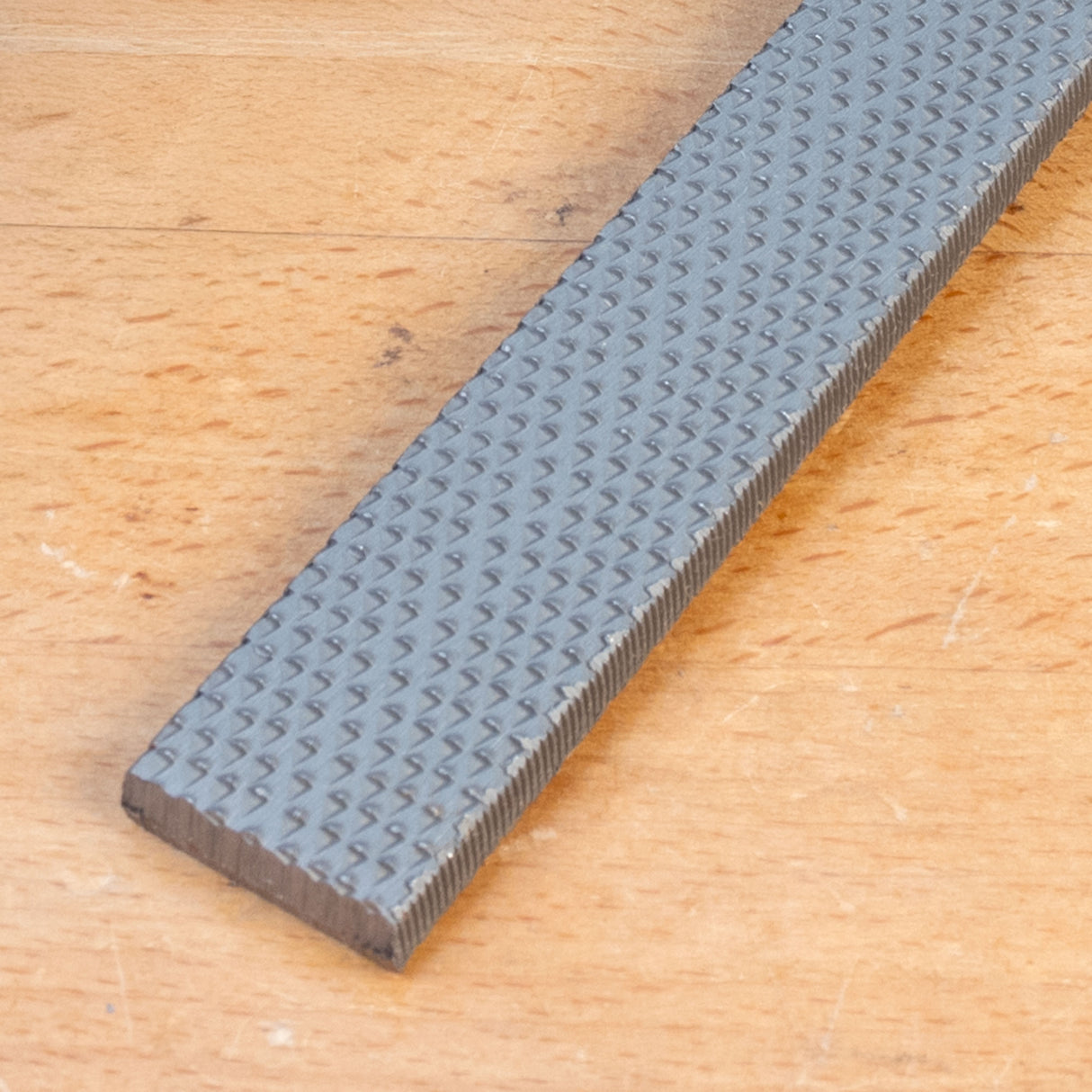 Flat chisel with textured steel blade on wooden surface, woodworking tool closeup