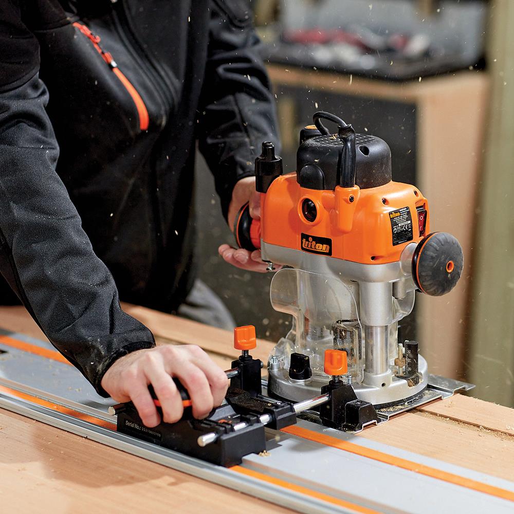 Woodworker using an orange plunge router on a guide rail for precise woodworking cuts