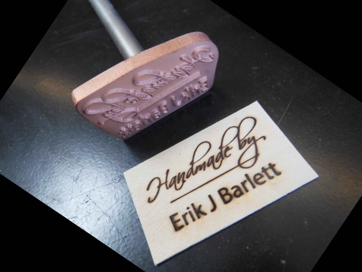 Custom wood branding iron tool beside engraved wooden nameplate on a dark surface