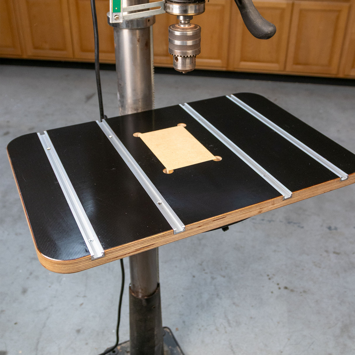Drill press table with T-tracks and insert for woodworking, mounted in a workshop