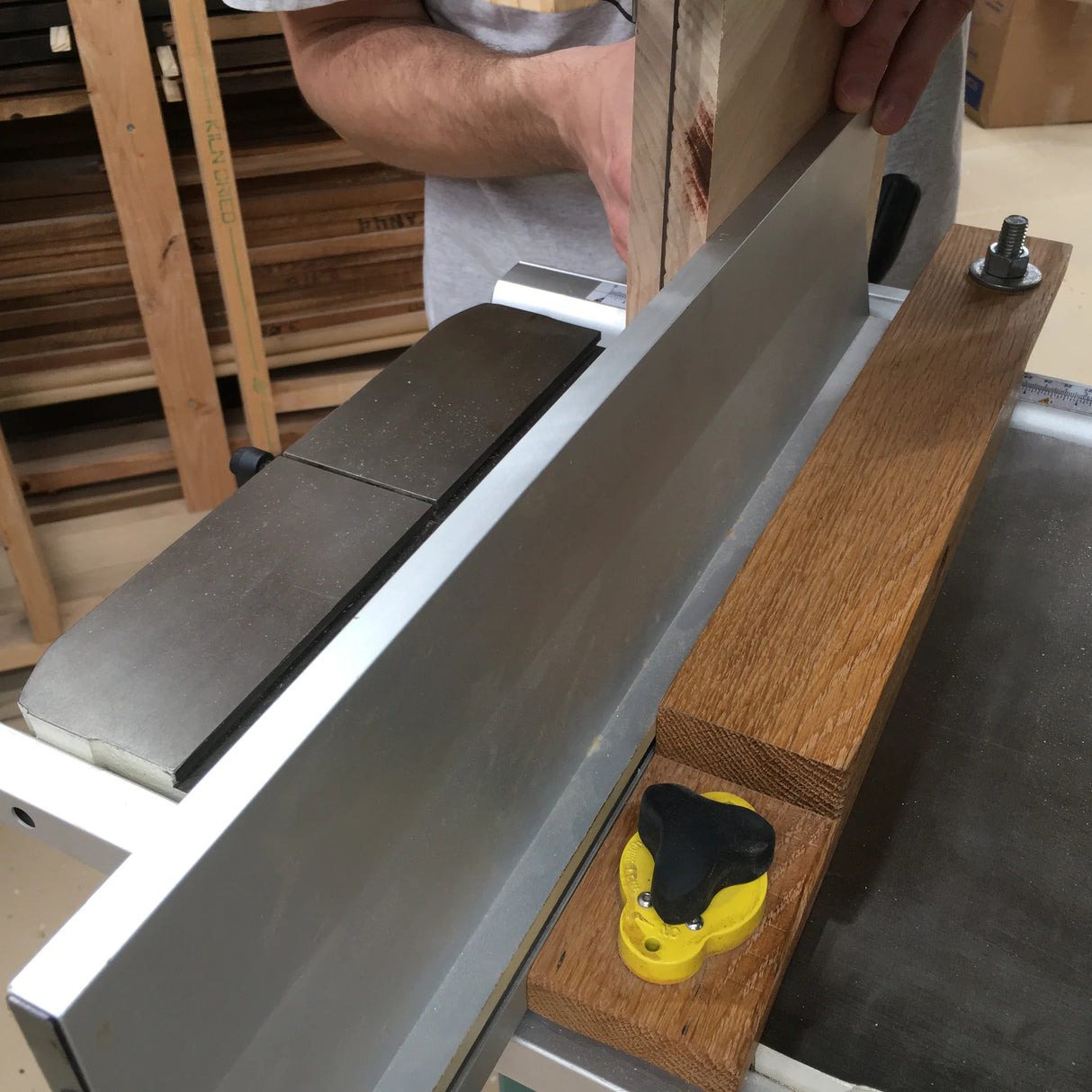 Woodworker using jointer and fence jig to square board edge in workshop