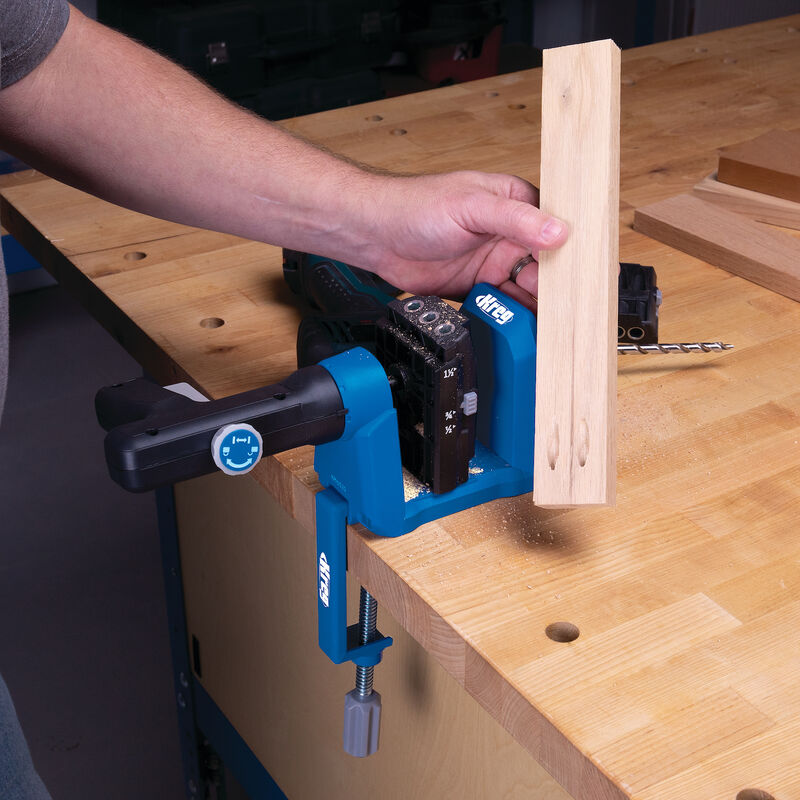 Pocket hole jig kit clamped to workbench with drilled wood piece and drill bit