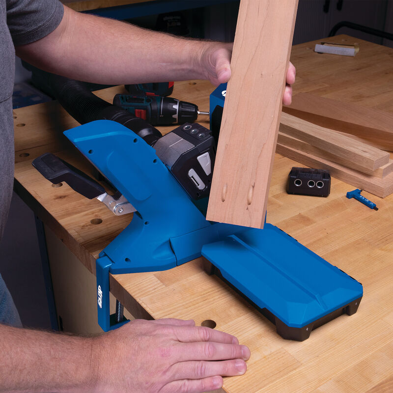 Woodworker using blue pocket hole jig system to drill angled holes in a wood board on workbench