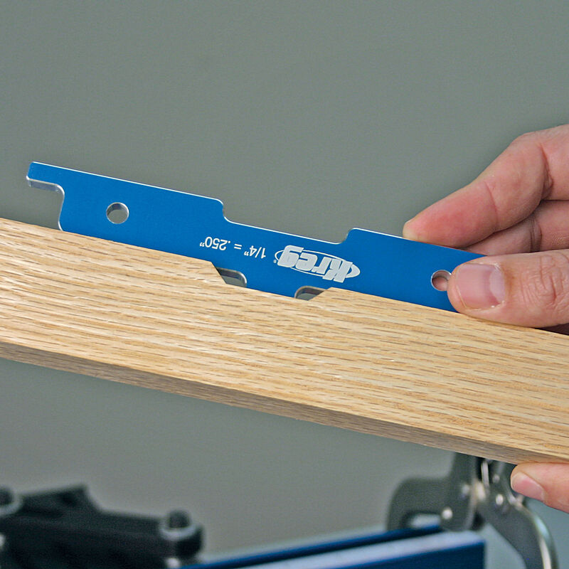 Blue router setup gauge being used to check a wood joint for precise woodworking alignment.