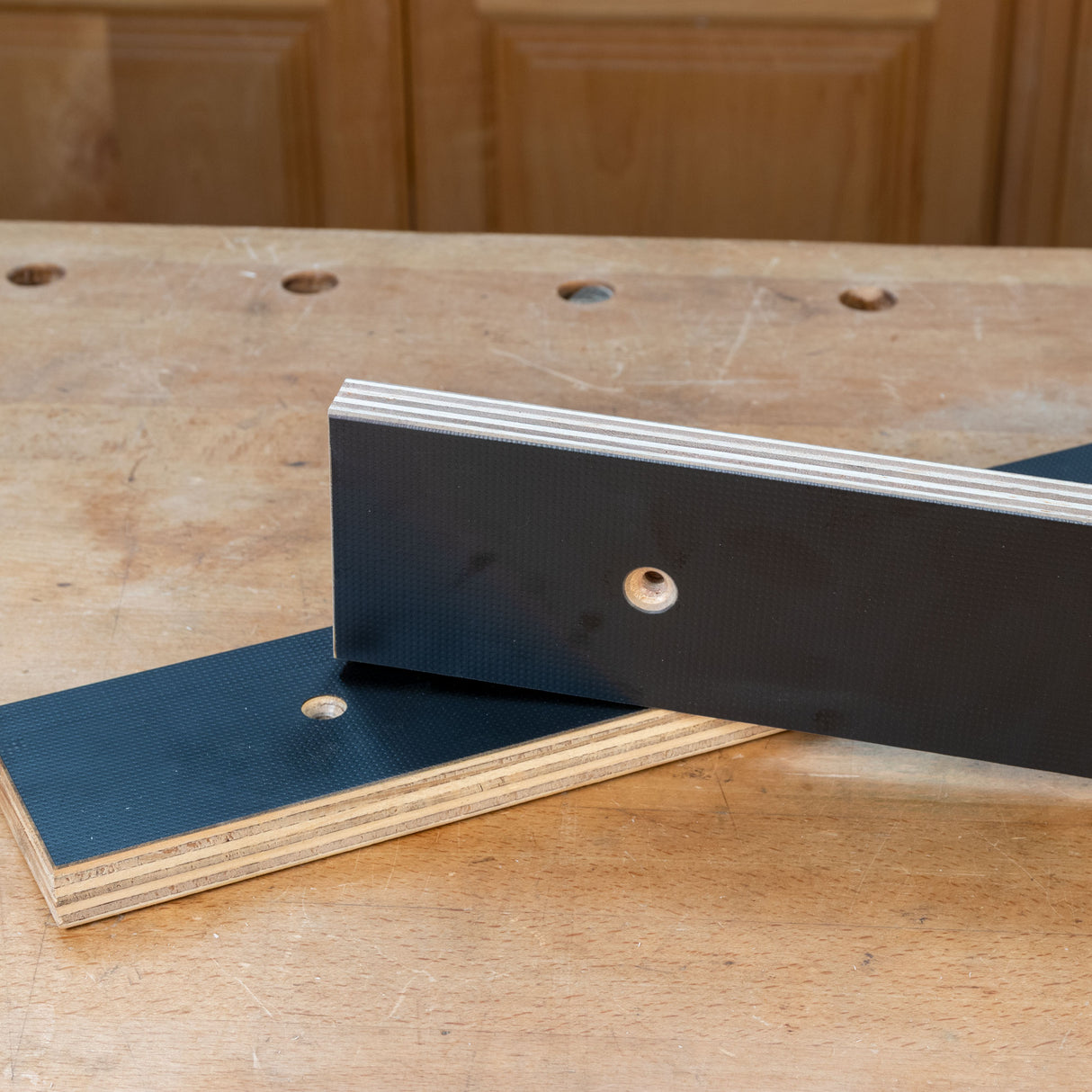 Close-up of two MDF phenolic bench dog plates with mounting holes on a woodworking table.