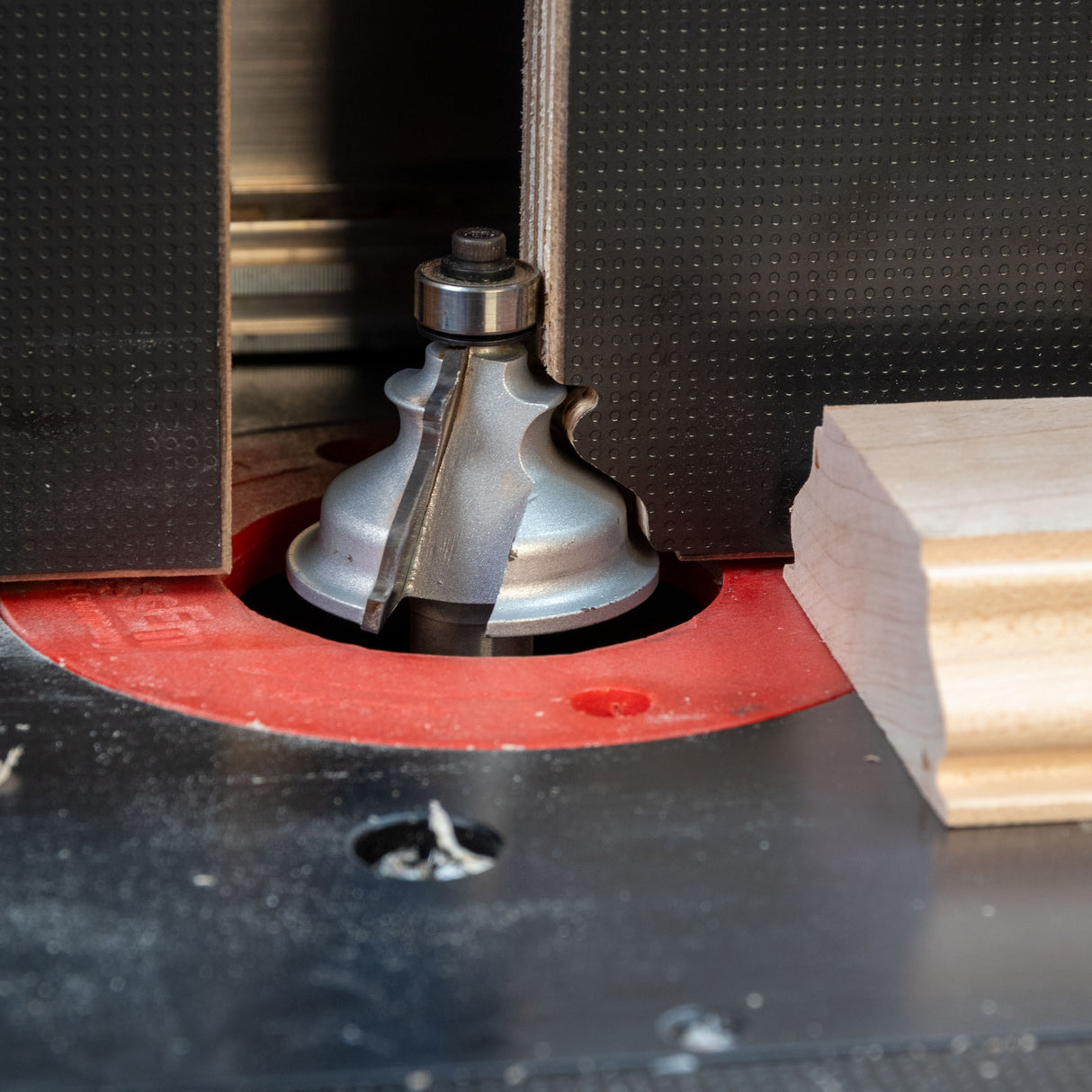 Close-up of a router table with roundover router bit cutting molding profile on wood piece