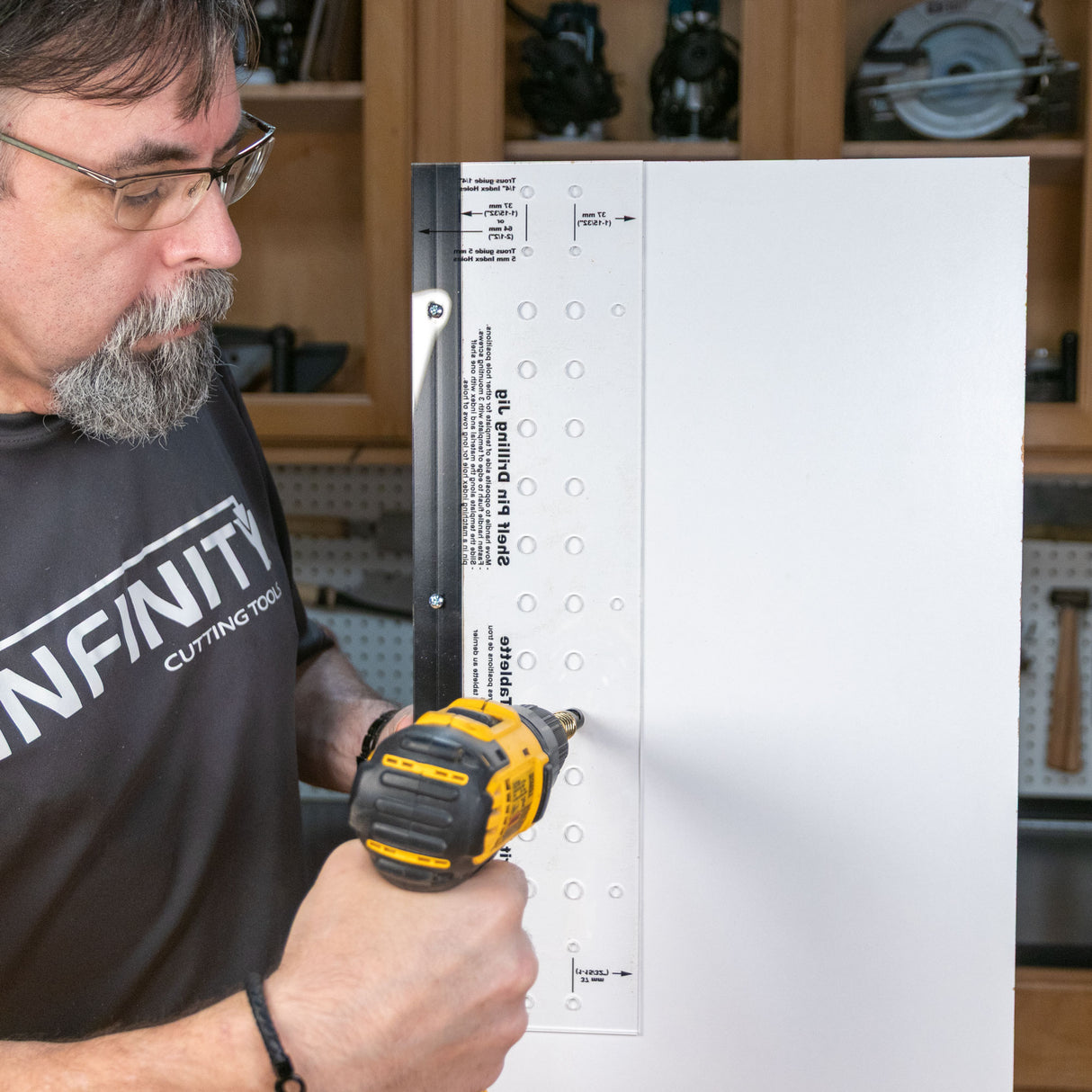 Man using a drill and shelf pin jig to make evenly spaced shelf holes on a wood panel