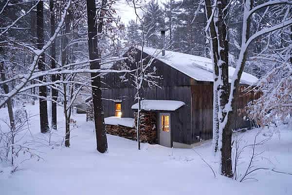Woodshop cabin surrounded by snowy forest, winter setting, warm lights glowing inside.