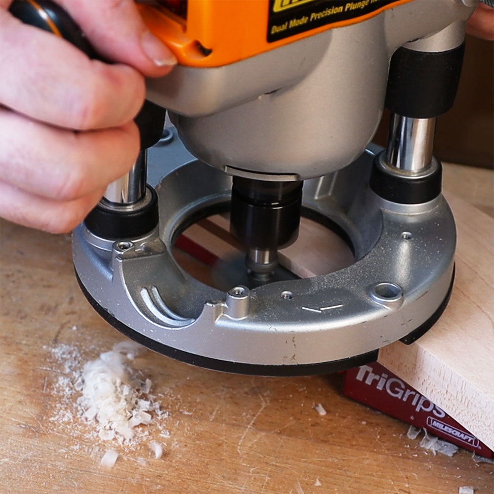 Wood router with slot cutter arbor in use on a wooden board, producing sawdust