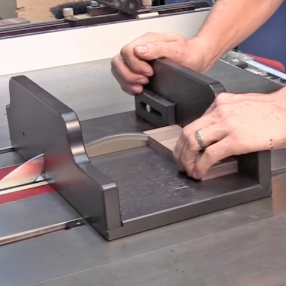 Woodworker using a table saw sled jig to cut a wooden block safely and accurately.