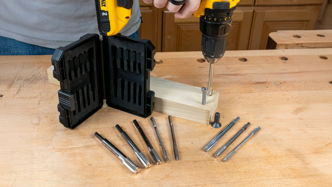 Woodworking tap and die set with case, drill, and metal taps on workbench