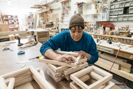 Woman carpenter assembling wooden cabinet frames in a busy woodworking shop