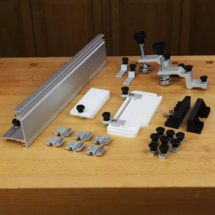 Router table accessory kit with fence, featherboard, clamps, knobs, and mounting hardware on a workbench.