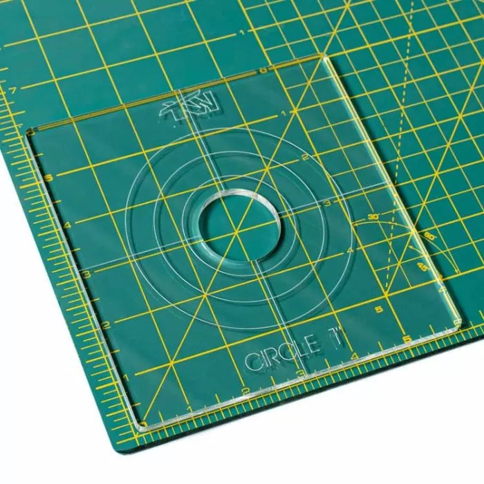 Acrylic circle router template on a green cutting mat with yellow grid lines for woodworking.
