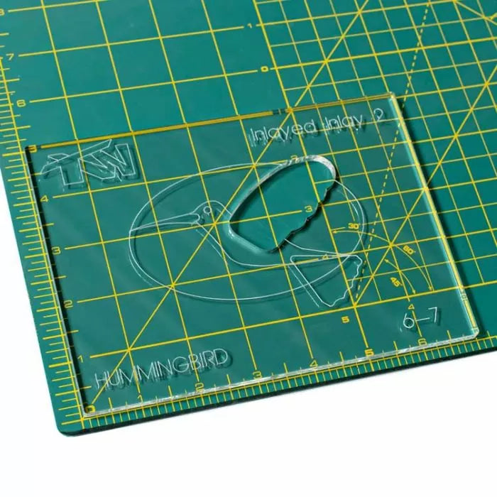 Acrylic inlay template with hummingbird design on a cutting mat for woodworking projects