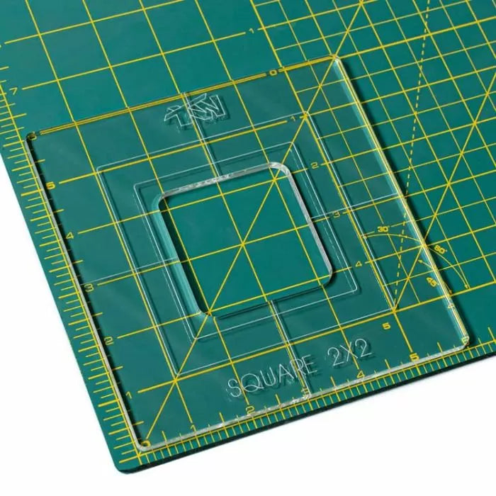Acrylic square quilting ruler template on a green gridded cutting mat, marked with measurements.