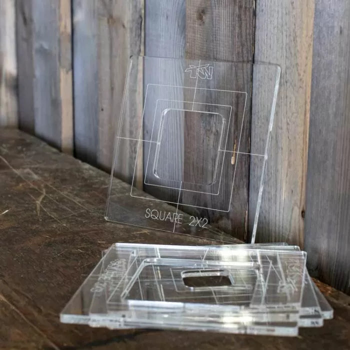 Clear acrylic router templates with square cutouts for woodworking, displayed on a rustic table