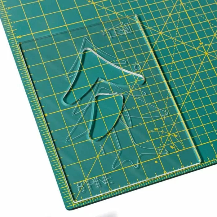 Acrylic woodworking template with tree shapes on a green cutting mat with yellow grid lines.