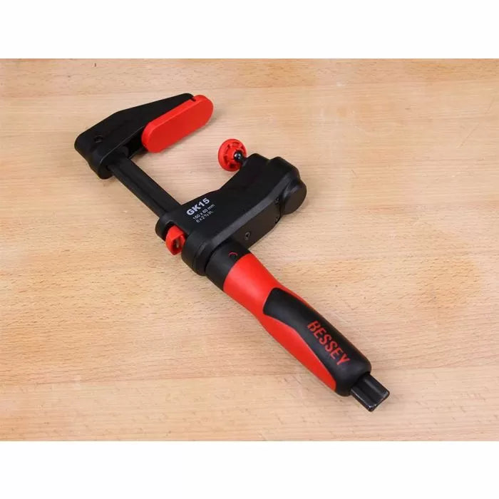 Bessey woodworking clamp with red and black handle on a wooden surface