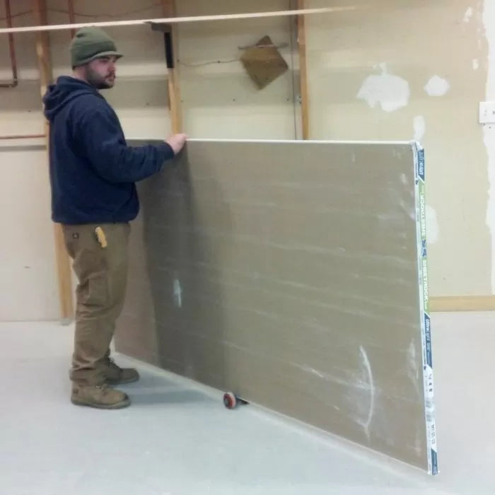Man moving drywall sheet on a roller tool in a woodworking or construction workshop