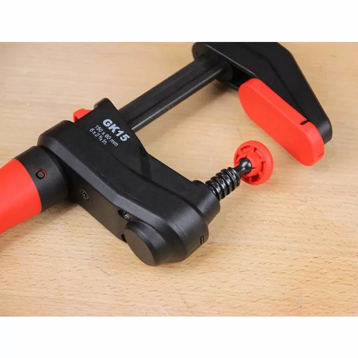 Close-up of a black and red woodworking clamp with GK15 markings on a wooden surface