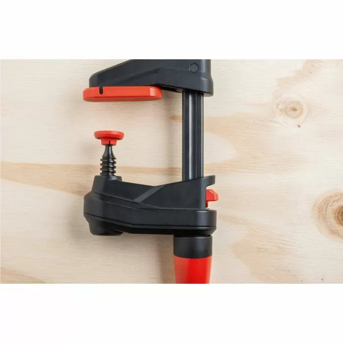 Woodworking clamp with red and black handles secured to a light wood surface